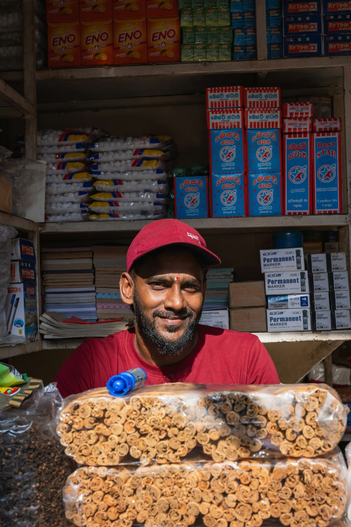 A corner-store owner smiling behind his counter.